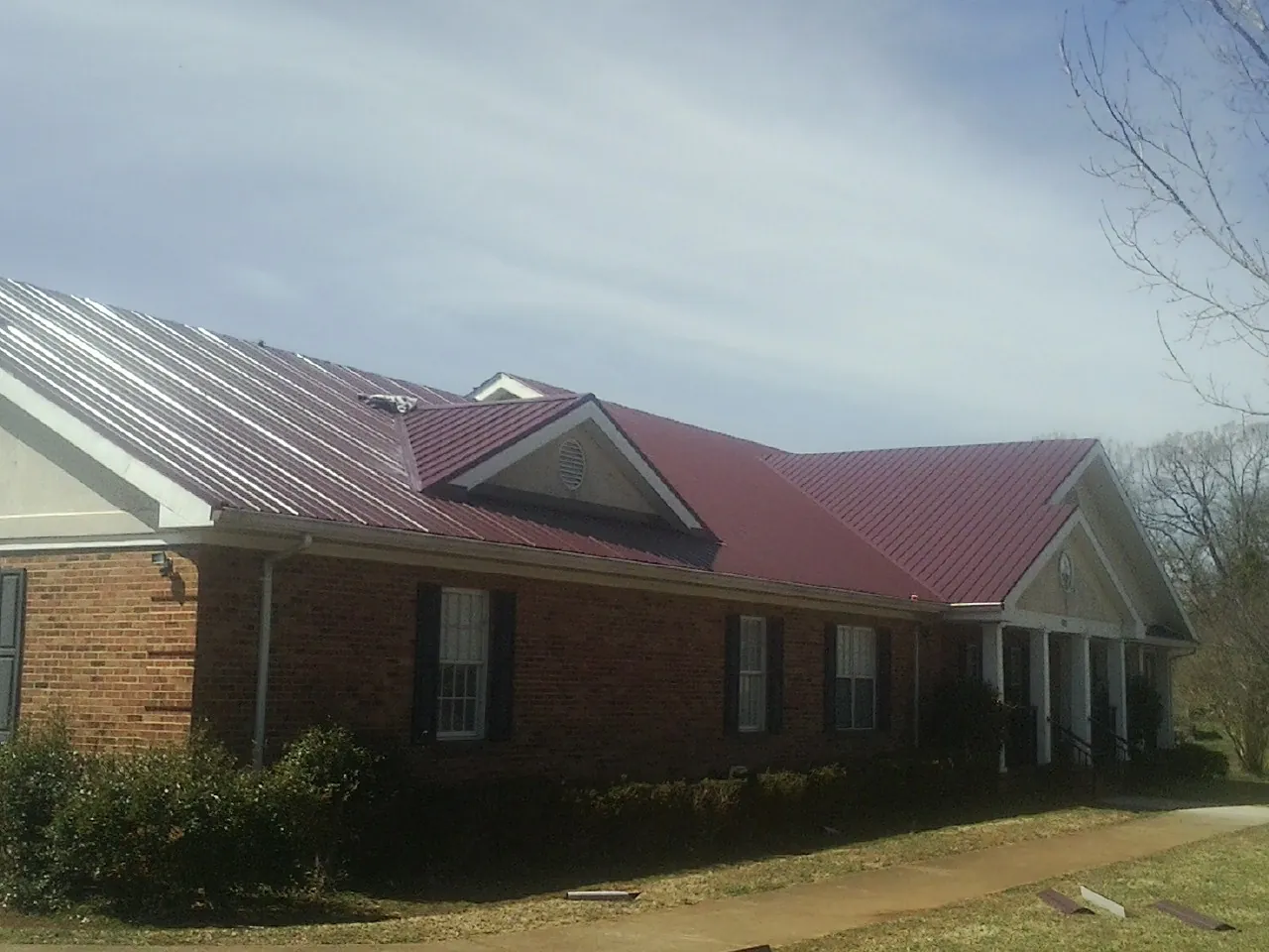 Red metal roof with gabled entries on a long brick building, from a Hail Damage Roof Repair job in Patrick Air Force Base