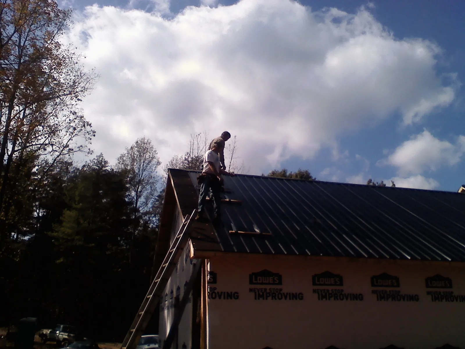 Roofer fastening dark metal panels high against a cloudy sky, from a Roof Inspection job in Patrick Air Force Base