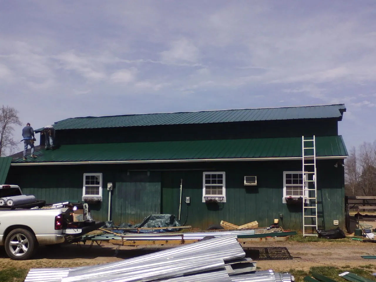 Crew installing green metal roofing on a large green barn in Patrick Air Force Base